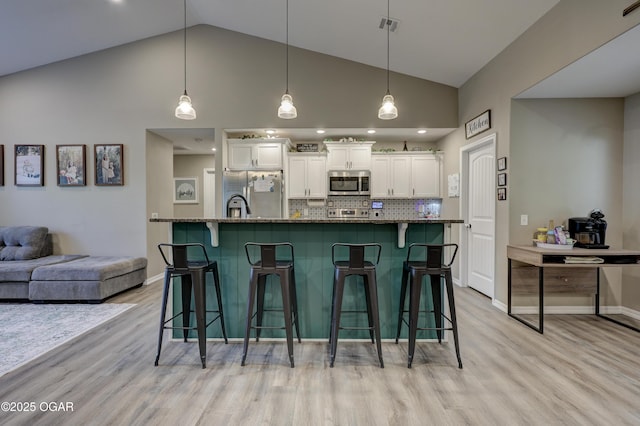 2615 E Xenia St, Joplin, MO 64801 - kitchen with appliances with stainless steel finishes, a breakfast bar area, white cabinetry, light wood-style floors, and high vaulted ceiling