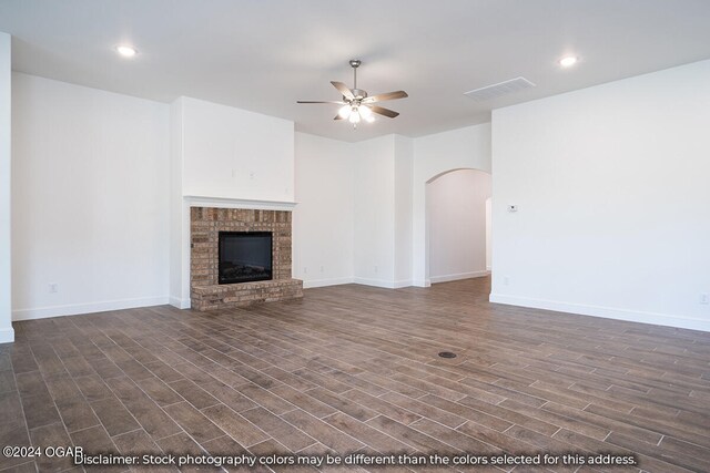 1507 E White Oak St, Joplin, MO 64801 - unfurnished living room featuring ceiling fan, dark wood-type flooring, arched walkways, a brick fireplace, and baseboards