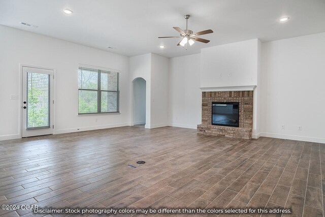 1507 E White Oak St, Joplin, MO 64801 - unfurnished living room featuring a ceiling fan, dark wood-type flooring, arched walkways, a brick fireplace, and baseboards