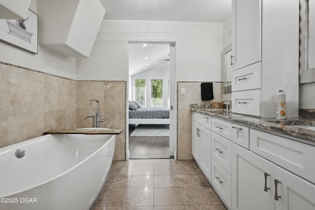 5594 Riverside Dr, Joplin, MO 64804 - full bathroom with tile walls, a freestanding bath, double vanity, ensuite bath, and vaulted ceiling
