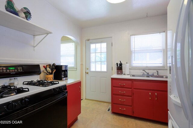 430 N Jackson Ave, Joplin, MO 64801 - kitchen featuring red cabinets, gas range oven, freestanding refrigerator, a sink, and arched walkways