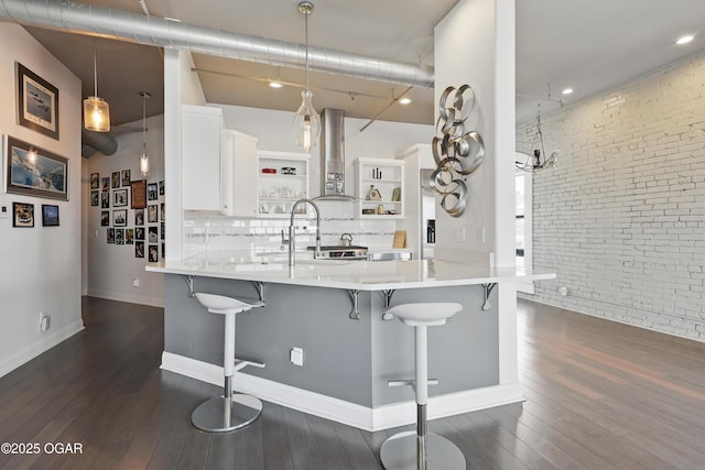 214 E 4th St Unit 402, Joplin, MO 64801 - kitchen featuring open shelves, brick wall, dark wood-type flooring, wall chimney exhaust hood, and a breakfast bar area