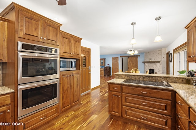 3431 Hawthorn Dr, Joplin, MO 64804 - kitchen featuring appliances with stainless steel finishes, wood finished floors, brown cabinets, decorative light fixtures, and light stone counters