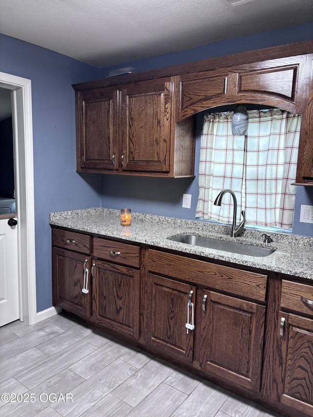 324 W Hill St, Neosho, MO 64850 - kitchen featuring a sink, light wood-style floors, dark brown cabinetry, and light stone countertops