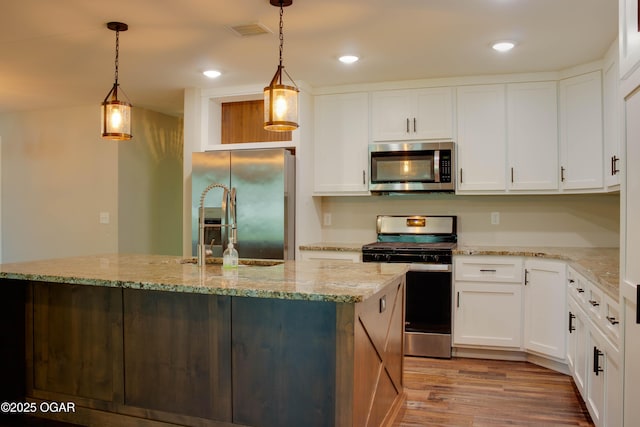 1002 S Mill St, Grove, OK 74344 - kitchen with appliances with stainless steel finishes, wood finished floors, white cabinets, a center island with sink, and recessed lighting