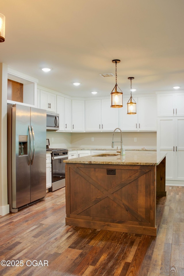 1002 S Mill St, Grove, OK 74344 - kitchen with appliances with stainless steel finishes, a sink, wood finished floors, white cabinetry, and hanging light fixtures