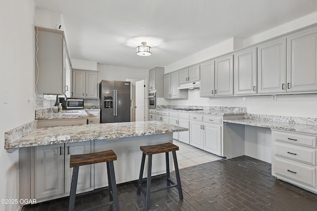 2722 Wisconsin Ave, Joplin, MO 64804 - kitchen featuring stainless steel appliances, under cabinet range hood, a peninsula, a kitchen bar, and light stone countertops