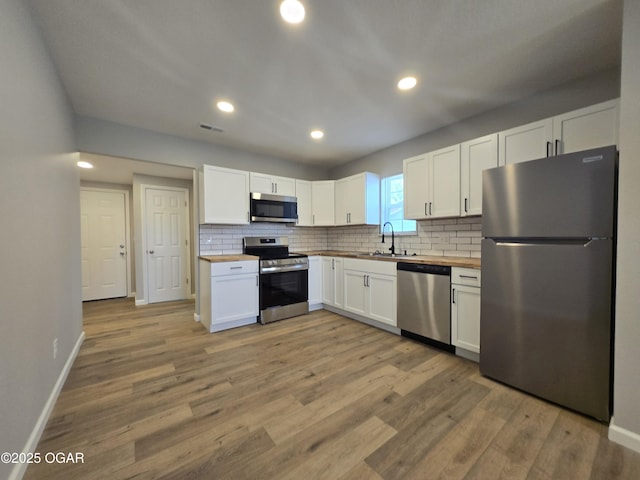 504 S Mckinley Ave, Joplin, MO 64801 - kitchen with stainless steel appliances, wood counters, decorative backsplash, white cabinetry, and light wood-style flooring