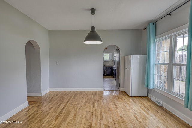2502 S Tyler Ave, Joplin, MO 64804 - unfurnished dining area with arched walkways, light wood finished floors, and baseboards