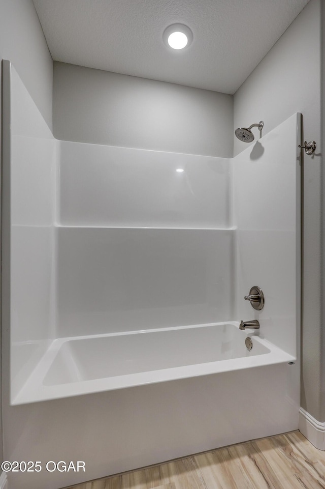full bath featuring wood finished floors, bathing tub / shower combination, and a textured ceiling