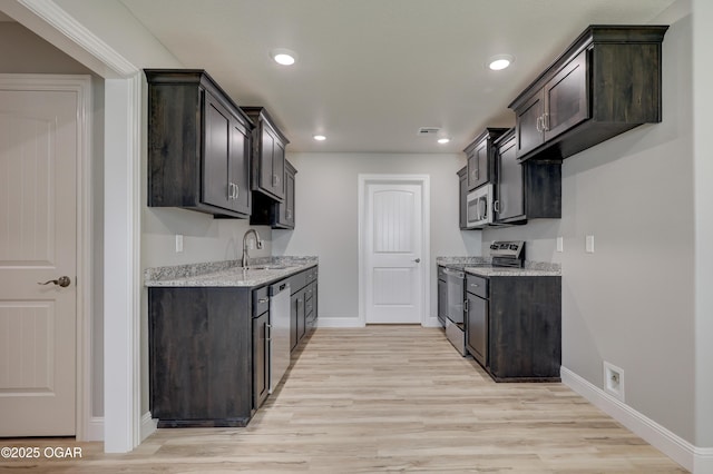 kitchen featuring appliances with stainless steel finishes, dark brown cabinets, light wood finished floors, and recessed lighting