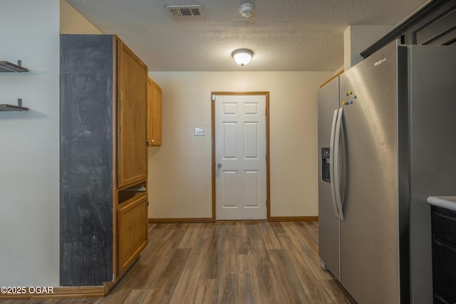 522 E Yale St, Liberal, MO 64762 - kitchen with stainless steel fridge, wood finished floors, a textured ceiling, brown cabinetry, and baseboards