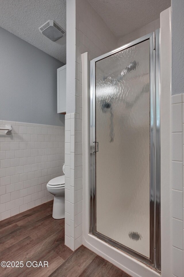 720 Sheridan Ave, Carl Junction, MO 64834 - bathroom featuring tile walls, wood finished floors, toilet, a textured ceiling, and a stall shower