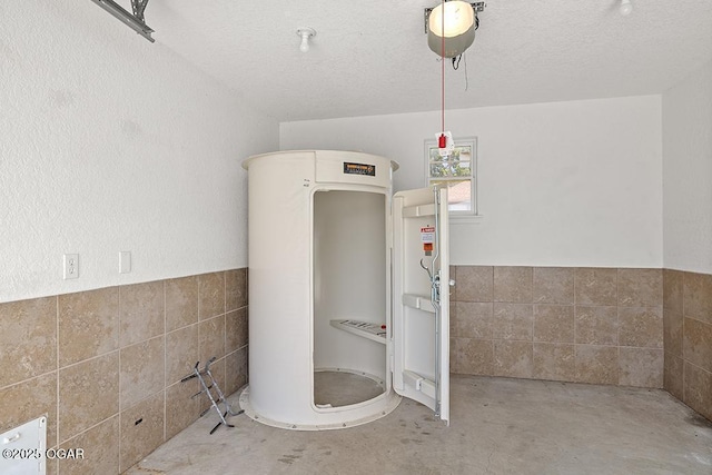 111 Zachary Ln, Carl Junction, MO 64834 - bathroom featuring tankless water heater, tile walls, concrete flooring, a textured ceiling, and a wainscoted wall