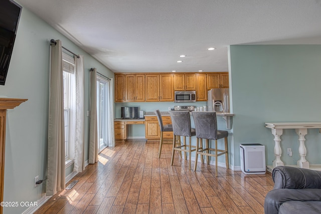 408 W Walton Ave, Carl Junction, MO 64834 - kitchen with stainless steel appliances, a breakfast bar, hardwood / wood-style floors, recessed lighting, and brown cabinetry