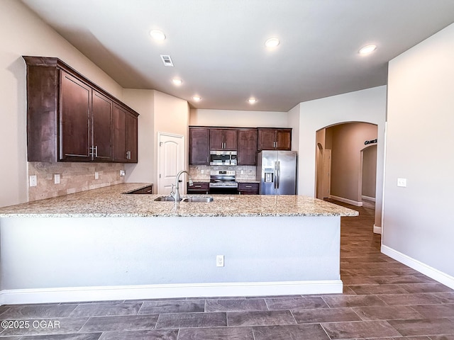 815 Delaney Dr, Carl Junction, MO 64834 - kitchen with appliances with stainless steel finishes, arched walkways, dark brown cabinets, a peninsula, and tasteful backsplash