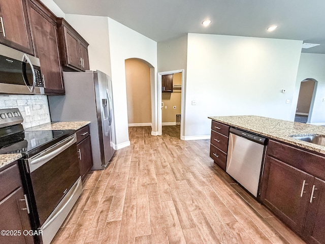 815 Delaney Dr, Carl Junction, MO 64834 - kitchen featuring stainless steel appliances, arched walkways, light wood-style flooring, light stone counters, and dark brown cabinets