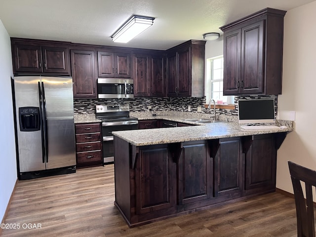 2038 W Trolley Car Ln, Carthage, MO 64836 - kitchen featuring appliances with stainless steel finishes, a peninsula, tasteful backsplash, dark brown cabinets, and wood finished floors