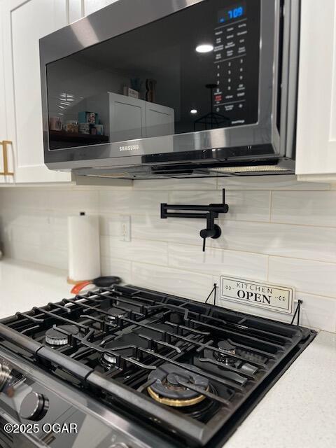 3331 Willow Ln, Joplin, MO 64801 - detailed view of stainless steel microwave, decorative backsplash, pot filler, gas range, and white cabinetry