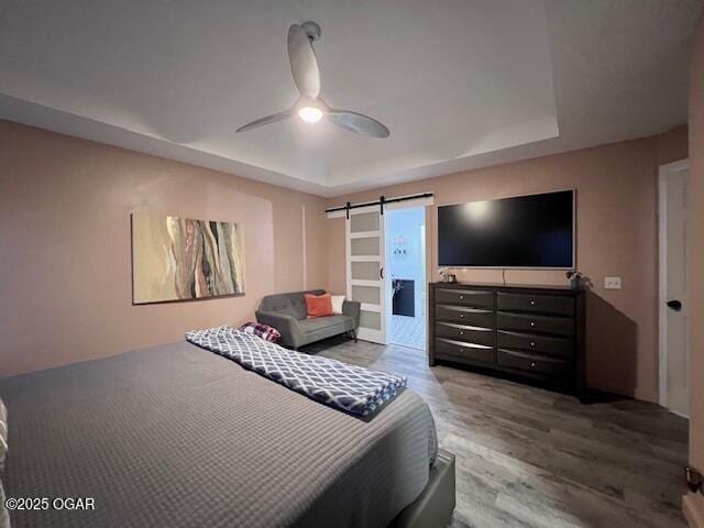 3331 Willow Ln, Joplin, MO 64801 - bedroom featuring a barn door, a tray ceiling, wood finished floors, and ceiling fan
