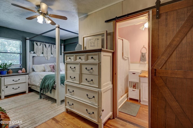509 Brentwood Dr, Carl Junction, MO 64834 - bedroom with a barn door, light wood-style floors, a textured ceiling, connected bathroom, and a ceiling fan