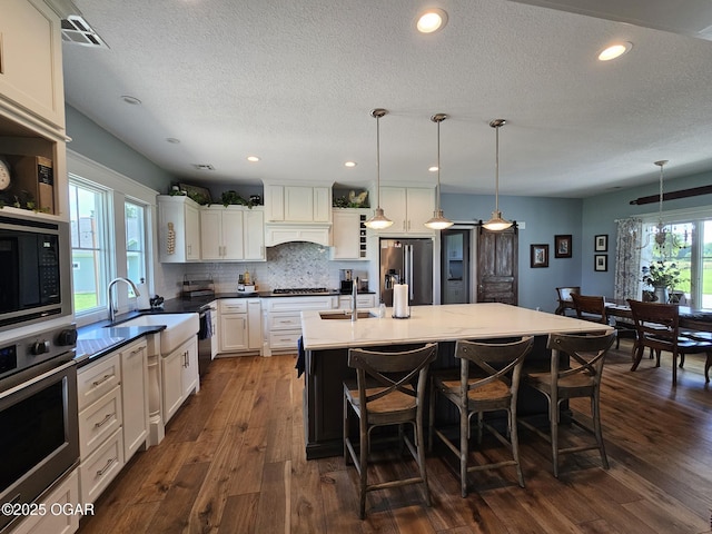 12673 Ibex Rd, Neosho, MO 64850 - kitchen with appliances with stainless steel finishes, a textured ceiling, a kitchen breakfast bar, dark wood-style flooring, and pendant lighting