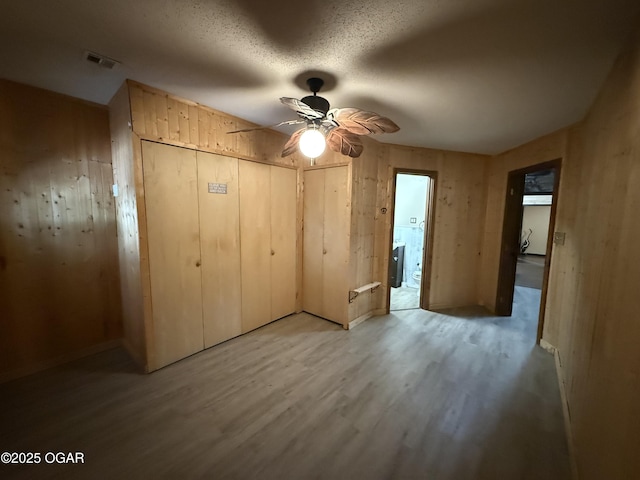 1310 Regan Ave, Carthage, MO 64836 - unfurnished bedroom featuring light wood-style floors, wooden walls, a ceiling fan, and a textured ceiling