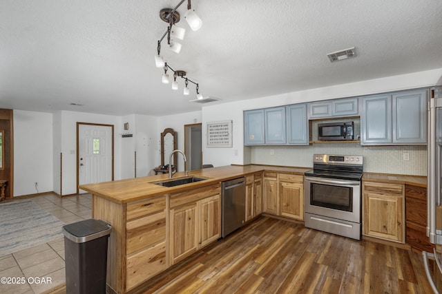 645 Worth St, Granby, MO 64844 - kitchen with appliances with stainless steel finishes, a peninsula, butcher block counters, rail lighting, and decorative backsplash