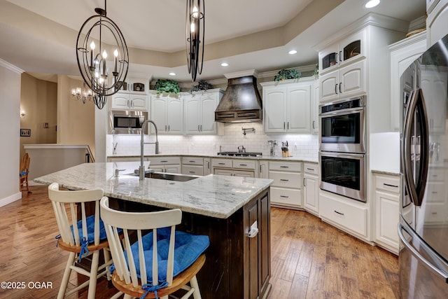 6133 Ridgeview Ct, Joplin, MO 64804 - kitchen featuring stainless steel appliances, custom exhaust hood, backsplash, an island with sink, and light wood-style floors