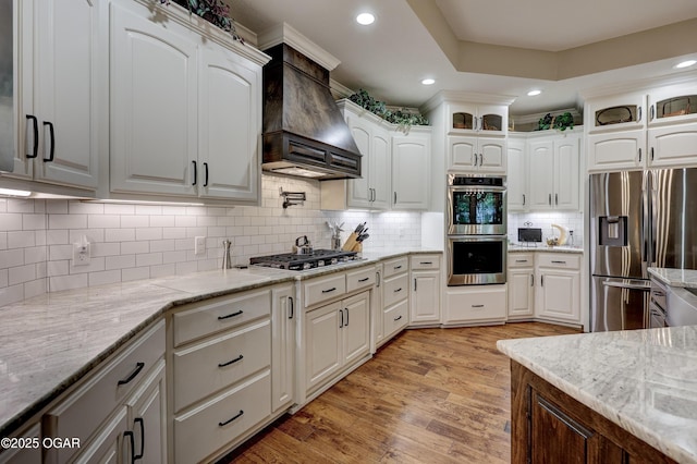 6133 Ridgeview Ct, Joplin, MO 64804 - kitchen featuring appliances with stainless steel finishes, custom exhaust hood, light wood-style flooring, white cabinets, and recessed lighting