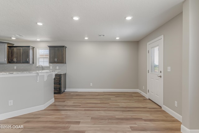 1220 Sheila Ann Dr, Carthage, MO 64836 - kitchen featuring a breakfast bar, decorative backsplash, light wood-style flooring, dark brown cabinetry, and recessed lighting