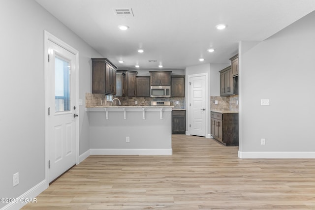 1224 Sheila Ann Dr, Carthage, MO 64836 - kitchen featuring stainless steel microwave, a peninsula, dark brown cabinets, decorative backsplash, and a breakfast bar area