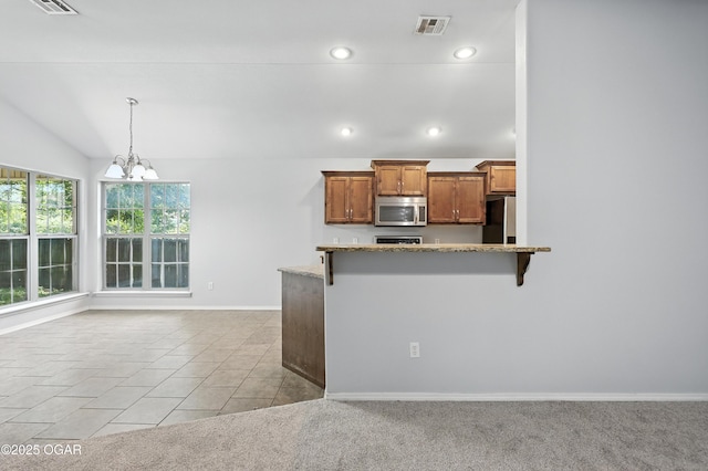 305 Anita Dr, Carl Junction, MO 64834 - kitchen with stainless steel microwave, freestanding refrigerator, a chandelier, brown cabinets, and a kitchen bar