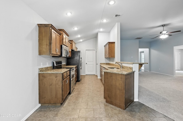 305 Anita Dr, Carl Junction, MO 64834 - kitchen featuring appliances with stainless steel finishes, a peninsula, brown cabinets, a breakfast bar, and light stone countertops