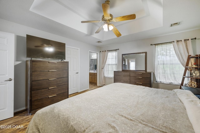 2238 Holly Ln, Miami, OK 74354 - bedroom featuring a raised ceiling, wood finished floors, ensuite bathroom, and a ceiling fan