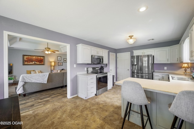 2238 Holly Ln, Miami, OK 74354 - kitchen featuring appliances with stainless steel finishes, a peninsula, light countertops, white cabinets, and a breakfast bar