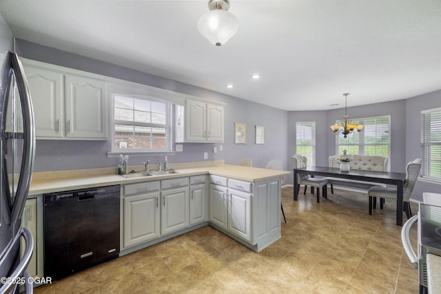 2238 Holly Ln, Miami, OK 74354 - kitchen with black dishwasher, freestanding refrigerator, a peninsula, a chandelier, and white cabinets