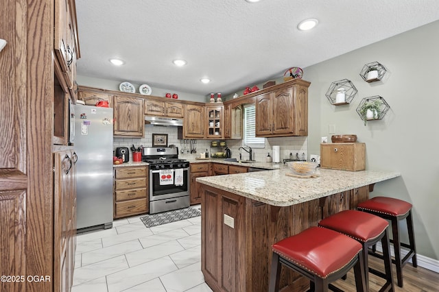 302 E 44th St, Joplin, MO 64804 - kitchen featuring stainless steel appliances, a peninsula, under cabinet range hood, a breakfast bar area, and a textured ceiling