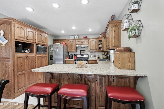 302 E 44th St, Joplin, MO 64804 - kitchen with appliances with stainless steel finishes, a peninsula, glass insert cabinets, backsplash, and light stone counters