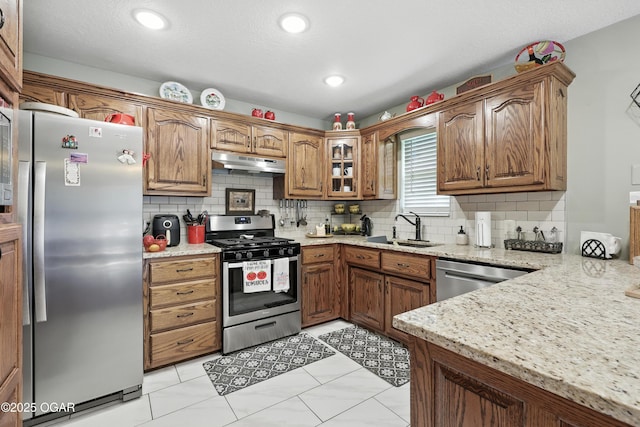 302 E 44th St, Joplin, MO 64804 - kitchen with stainless steel appliances, under cabinet range hood, tasteful backsplash, light stone countertops, and brown cabinets