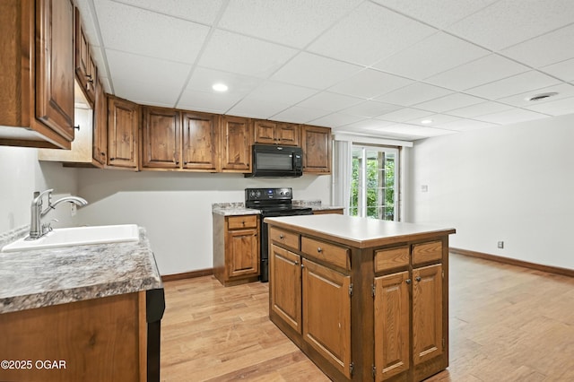 3310 Tana St, Joplin, MO 64804 - kitchen featuring black appliances, brown cabinetry, light wood-type flooring, a paneled ceiling, and light countertops