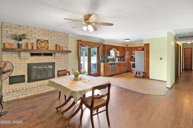 3508 Dirr Ave, Parsons, KS 67357 - dining space with ceiling fan, a brick fireplace, crown molding, light wood-type flooring, and a textured ceiling