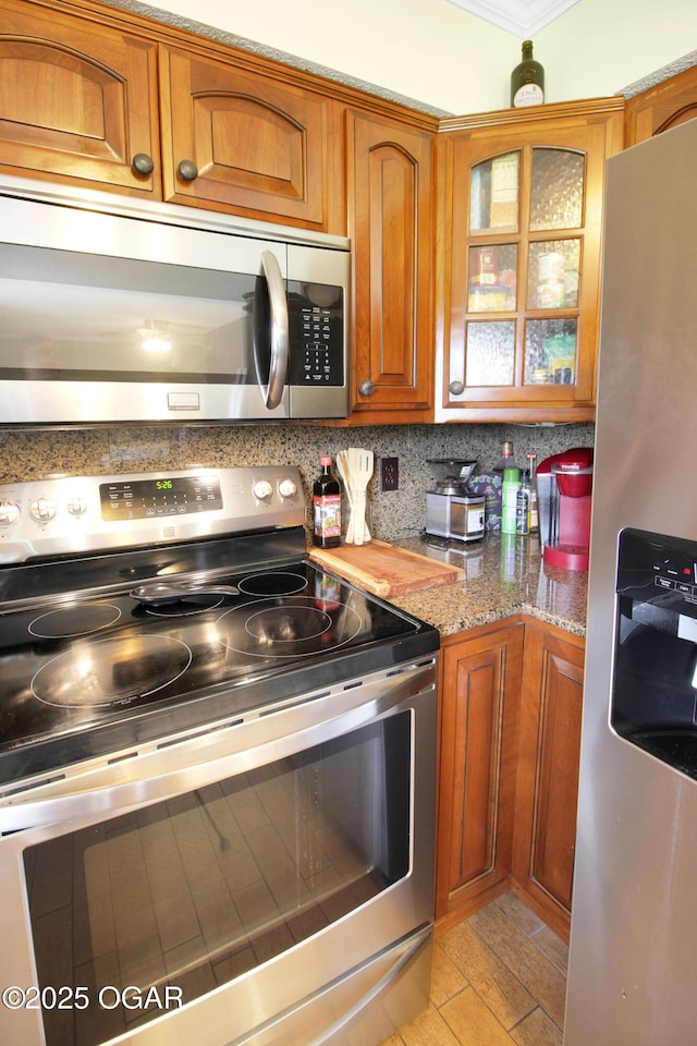 3508 Dirr Ave, Parsons, KS 67357 - kitchen with stainless steel appliances, brown cabinetry, decorative backsplash, glass insert cabinets, and light stone counters