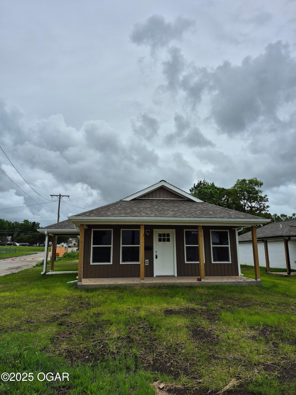 404 W Daugherty St, Carterville, MO 64835 - view of front of home with a porch, board and batten siding, a front yard, and roof with shingles