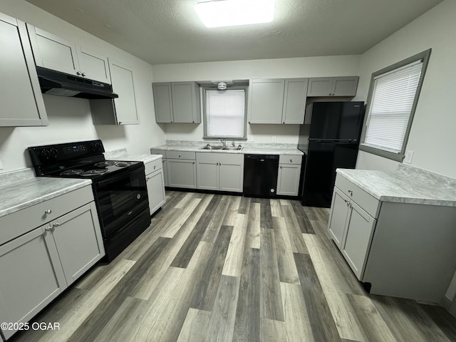 1003 Orchard St, Carthage, MO 64836 - kitchen with black appliances, under cabinet range hood, gray cabinetry, wood finished floors, and light countertops