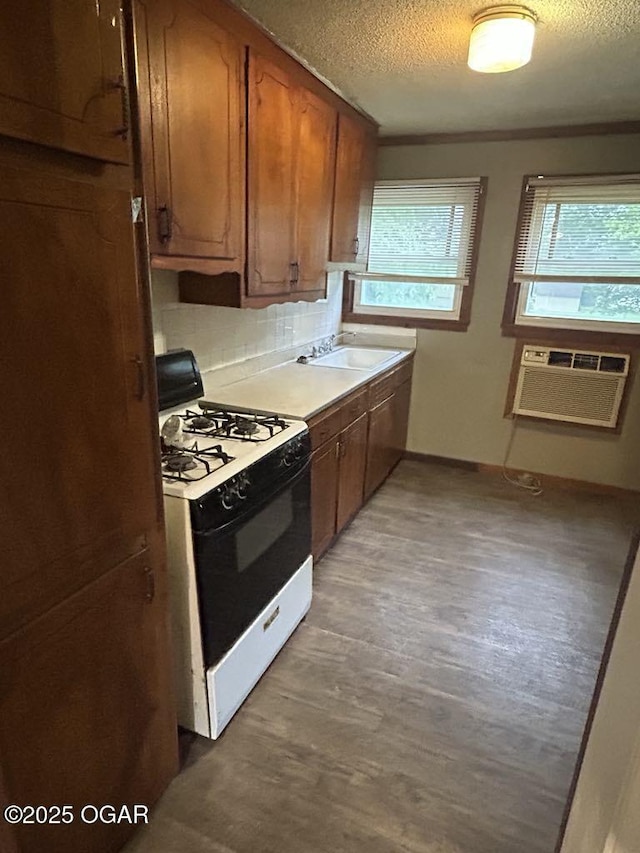419 Depot St, Oswego, KS 67356 - kitchen with white gas range oven, a wall mounted AC, a textured ceiling, brown cabinetry, and wood finished floors