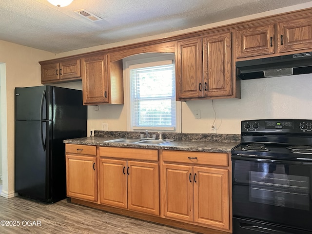 821 New Hampshire Ave, Joplin, MO 64801 - kitchen featuring black appliances, under cabinet range hood, dark countertops, light wood finished floors, and brown cabinetry