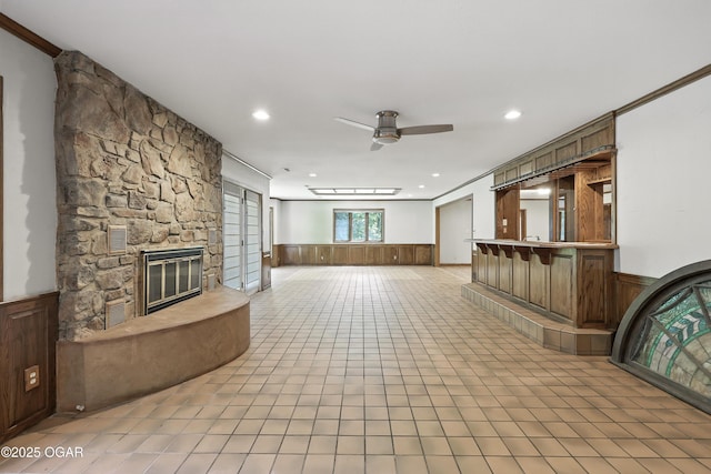 5623 Rivercrest Valley Dr, Joplin, MO 64804 - unfurnished living room featuring a ceiling fan, a wainscoted wall, recessed lighting, a stone fireplace, and light tile patterned flooring