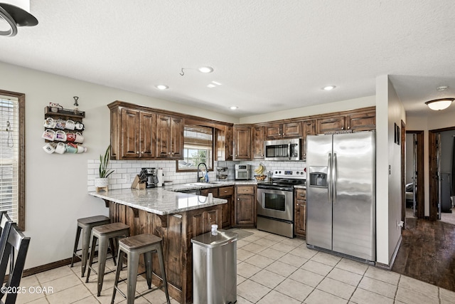2256 N Greystone Sq, Webb City, MO 64870 - kitchen featuring stainless steel appliances, a peninsula, tasteful backsplash, light stone counters, and a breakfast bar area