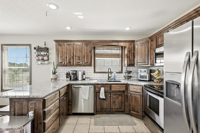 2256 N Greystone Sq, Webb City, MO 64870 - kitchen featuring stainless steel appliances, a peninsula, backsplash, dark brown cabinets, and light stone countertops
